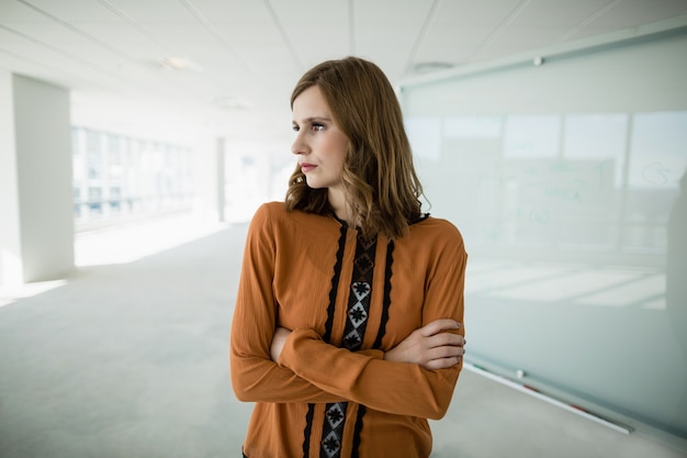 Business executive standing with arms crossed in office corridor