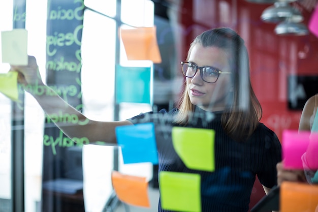 Business executive sticking sticky notes on glass