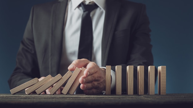 Photo business executive stopping collapsing dominos with his hand