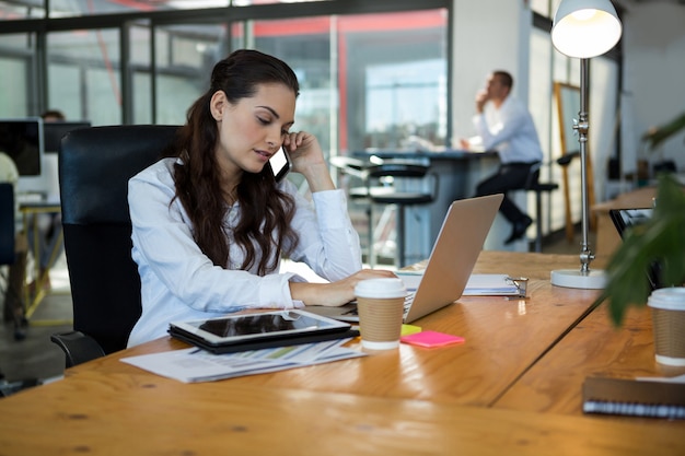 Business executive talking on mobile phone while using laptop at desk