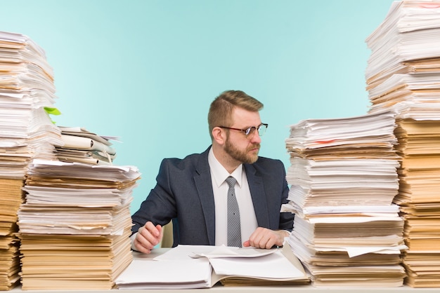 Business executive working in the office and piles of paperwork, he is overloaded with work -