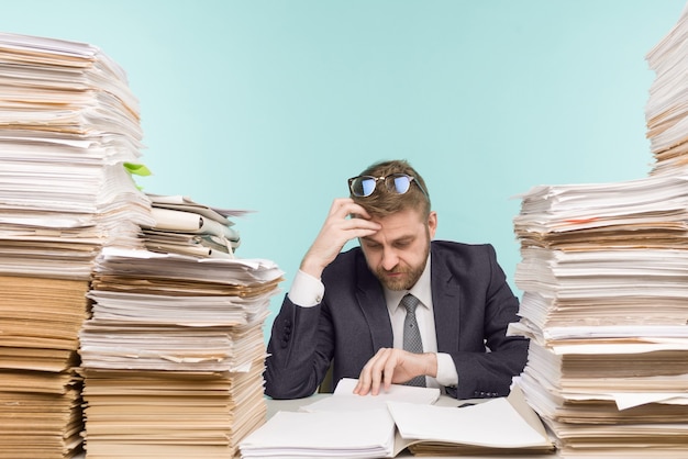 Business executive working in the office and piles of paperwork, he is overloaded with work -