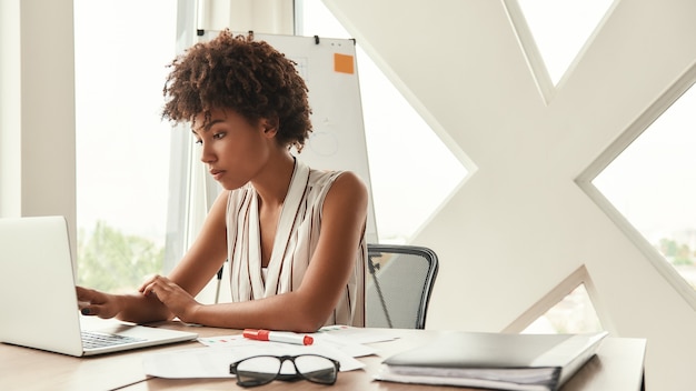 비즈니스 전문가. 현대적인 사무실에 앉아 노트북 작업을 하는 아름다운 아프리카계 미국인 여성. 비즈니스 개념입니다. 사무실 생활