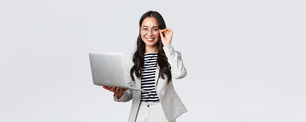 Business finance and employment female successful entrepreneurs concept Confident smiling asian businesswoman office worker in white suit and glasses using laptop help clients