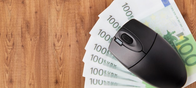 business, finance, internet earning and technology concept - close up of computer mouse and euro cash money on wooden table background