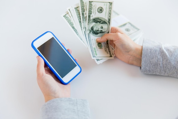 business, finance, saving, technology and people concept - close up of woman hands with smartphone and us dollar money