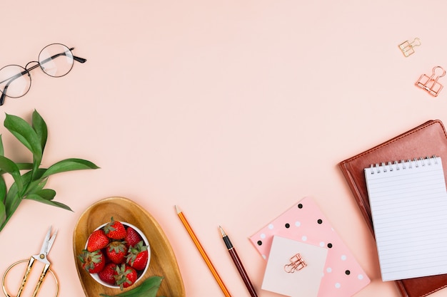 Business flatlay mockup with strawberries on a wooden tray, notebooks, glasses, ruscus branches and other accessories on pastel background with copyspace