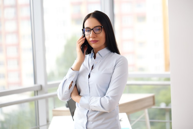 Business girl in a shirt by the window chats on the phone