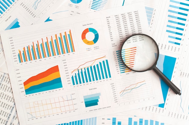 Business graphs charts and magnifying glass on table Financial development