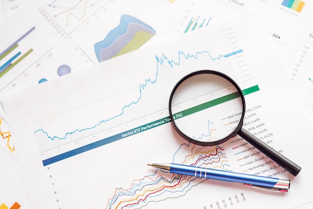 Premium Photo | Business graphs and magnifying glass with pen on table