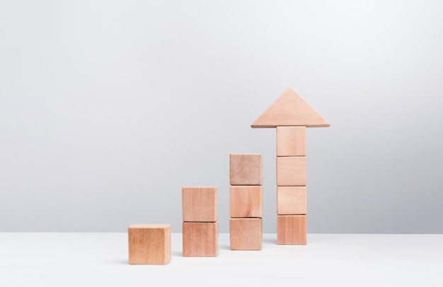 Business growth success concept. Wooden blocks stacking as an arrow up averages as a growth graph chart on white background, minimal and eco style.