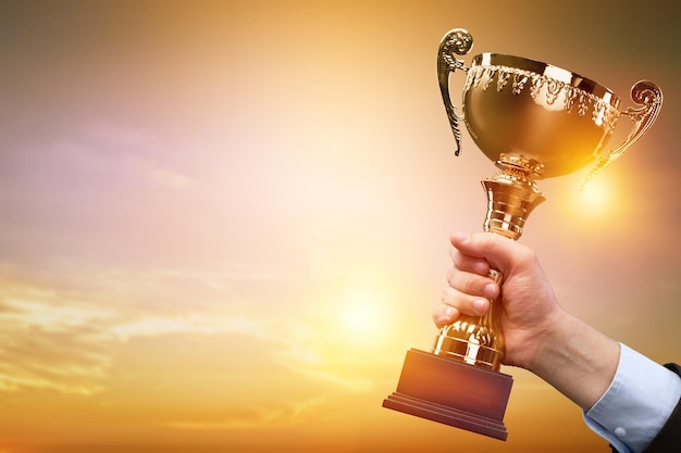 Business hands holding trophy cup on sunset background