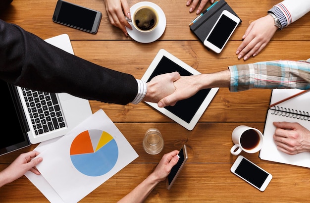 Business handshake at meeting, contract conclusion and successful agreement concept. Top view crop of hands at wooden table background