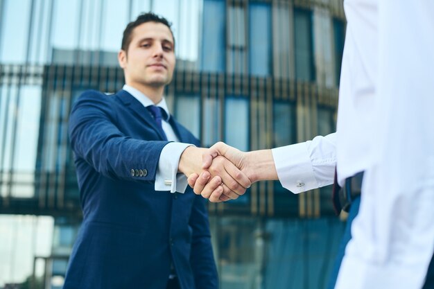 Business handshake outside of office building. Partnership meeting concept. Successful businessmen handshaking after good deal. low view