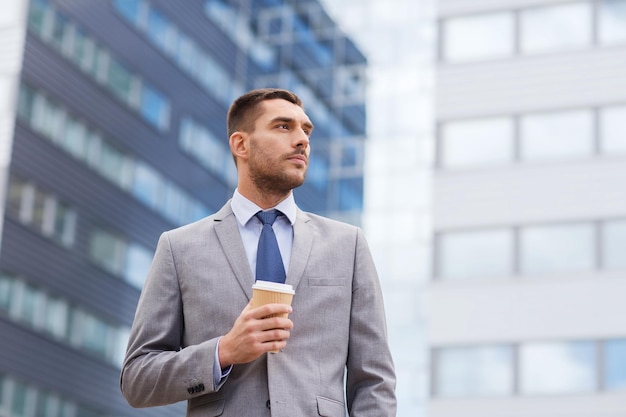 business, hot drinks and people and concept - young serious businessman with paper coffee cup over office building