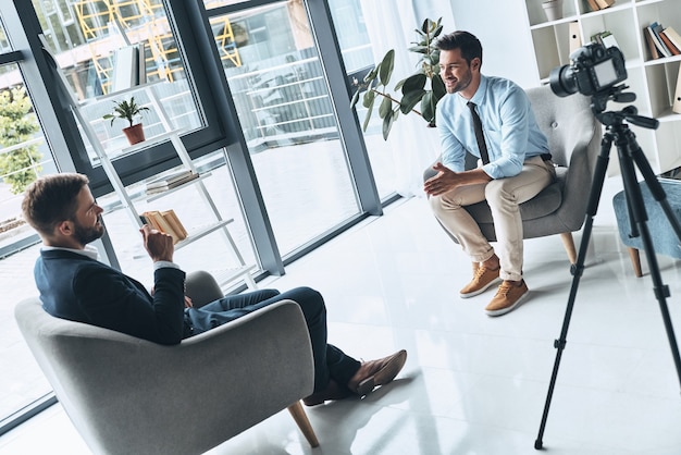 Business interview. Two young men in smart casual wear talking while making new video indoors