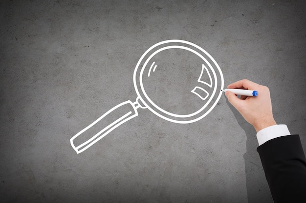 business and investigation concept - close up of businessman drawing magnifying glass on concrete wall