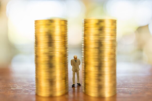 Business, Investment and Planning Concept.  Close up of  businessman miniature people figure standing between stack of gold coins on wooden table.