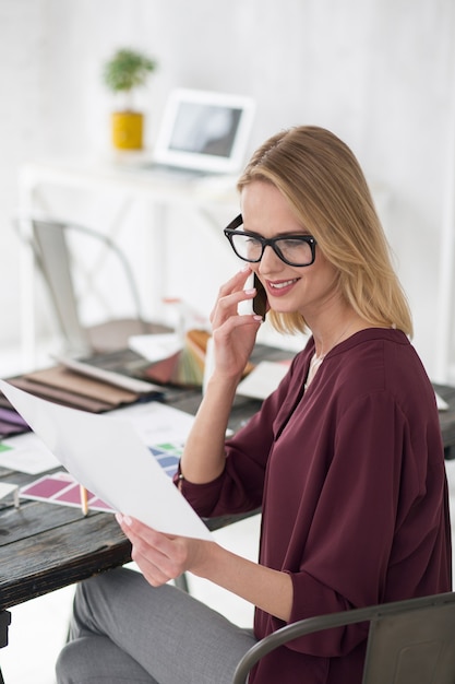 Business issue. Top view of cheerful nice businesswoman posing at table and using phone