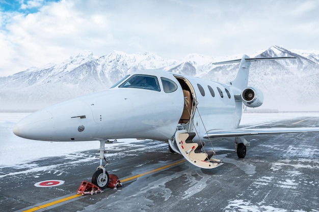 写真 高い雪で覆われた山の背景にある冬の空港でゲンゲイドアを開けたビジネスジェット機