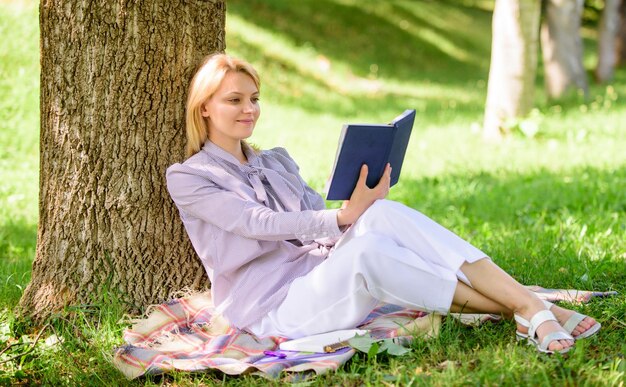 비즈니스 여성은 자신의 지식을 향상시키기 위해 책을 읽는 분을 찾습니다. 여성 자기 개선 소녀는 공원에 앉아 잔디에서 휴식을 취하는 동안 나무에 기대어 자기 개선 책 자기 개선 및 교육 개념