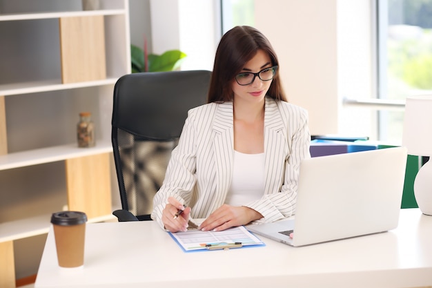 Business lady in a light jacket sitting at the table has a laptop