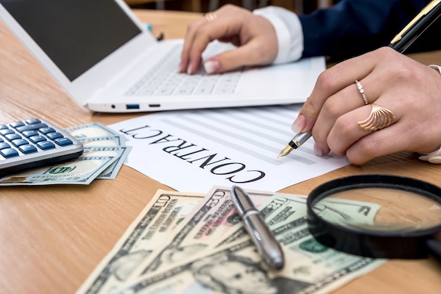 Business lady signs contract next to dollar banknotes calculator and pen