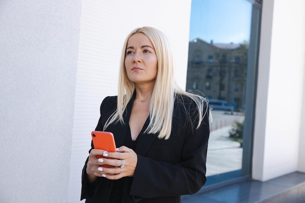 A business lady in a stylish suit with a phone poses on the street