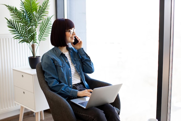 Business lady talking on phone while using laptop in office