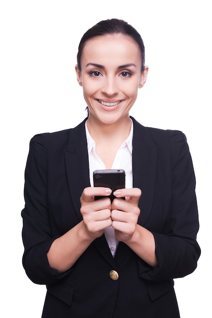 Business lady with mobile phone. Cheerful young woman in formalwear holding mobile phone and smiling while standing isolated on white