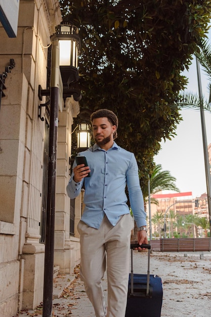 Business latin man with a suitcase and a mobile phone on the\
street