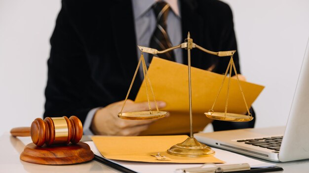 ビジネスと弁護士がオフィスの机の上で真鍮のスケールで契約書について話し合う法務サービスのアドバイス正義と法律の概念x9