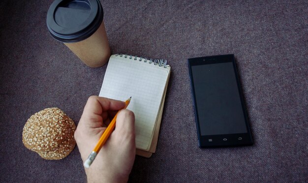 ビジネス、ライフスタイル、食べ物、人、コーヒーのコンセプト-茶色の生地の背景に鉛筆、ノートブック、紙のコーヒーカップ