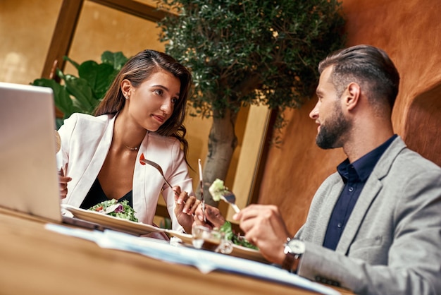 Pranzo di lavoro uomo e donna seduti a tavola al ristorante mangiando sana insalata fresca discutendo