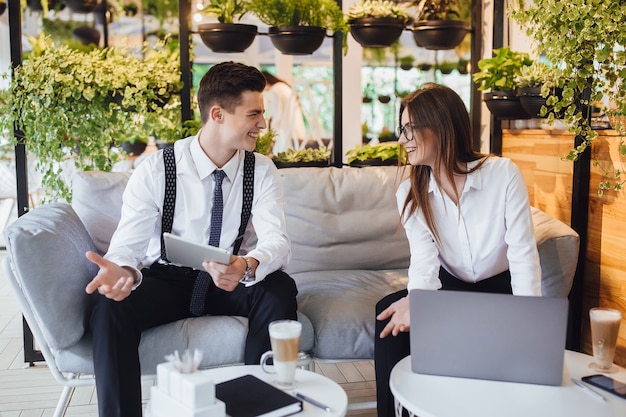 Business lunch! Two young people discuss a plan for a day in a cafe with laptops and a tablet