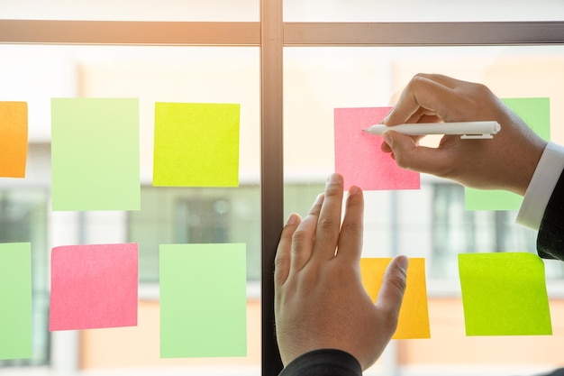 Business male writing note on the Colorful of post it on the wall. sticky note or paper note on the windows for note what to do in the office.