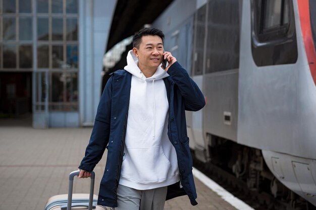 Uomo d'affari uomo asiatico alla stazione ferroviaria divertendosi a parlare al telefono un passeggero è arrivato in visita d'affari in una nuova città con una grande valigia di bagagli