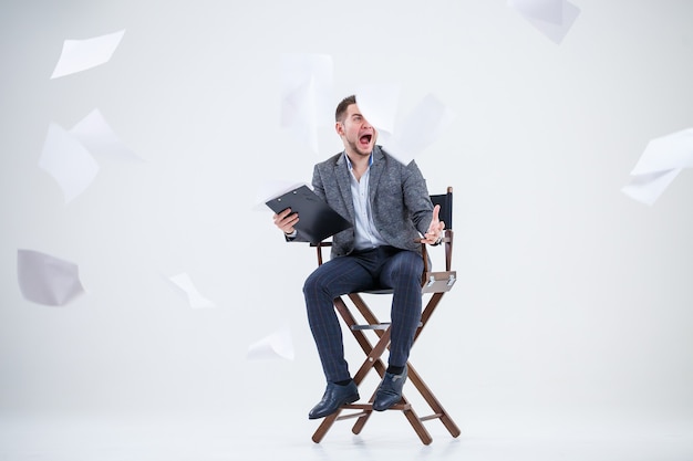 Business man businessman in a suit sitting on a wooden chair and throws documents. On a white background with thoughts of a new project