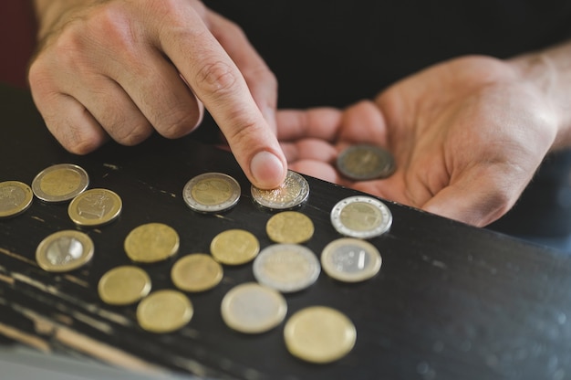 お金を数えるビジネスマン。金持ちの男性の手は、ラップトップの前のテーブルにさまざまなユーロのコインを持って数えます