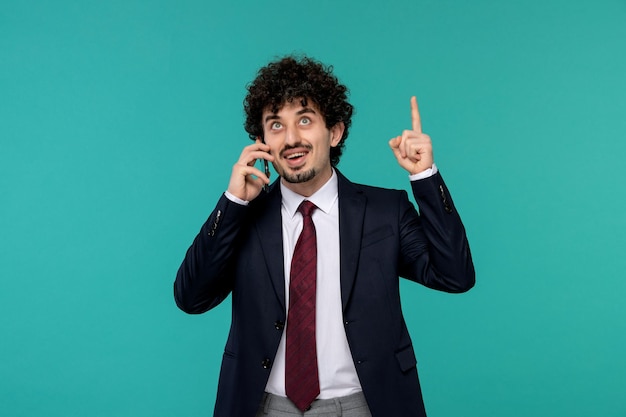 Business man curly cute handsome guy in black suit happily pointing up and holding phone