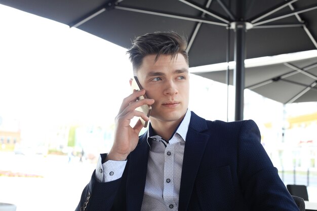 Business man drinking a cup of coffee while sitting with his phone in cafe.