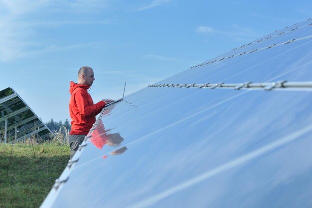 Foto ingegnere uomo d'affari che utilizza il computer portatile al campo di energia eco dell'impianto di pannelli solari in background