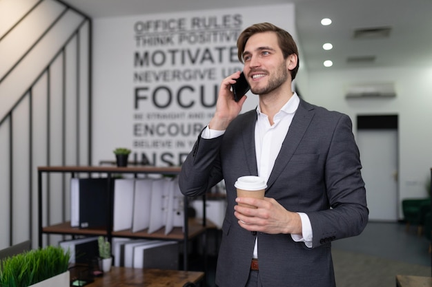 Business man in formal suit talking on the phone with a cup of coffee in his hands in the office