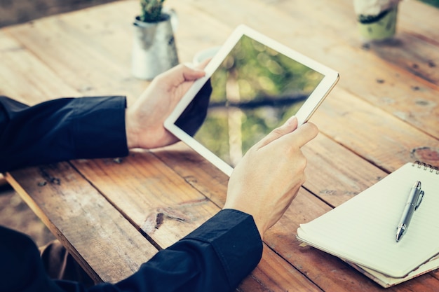 Photo business man hand holding tablet on table in coffee shop with vintage toned filter.