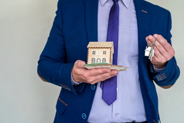 사업가는 집을 팔거나 임대하기 위해 유로화로 집 열쇠를 들고 있습니다. 구매 개념