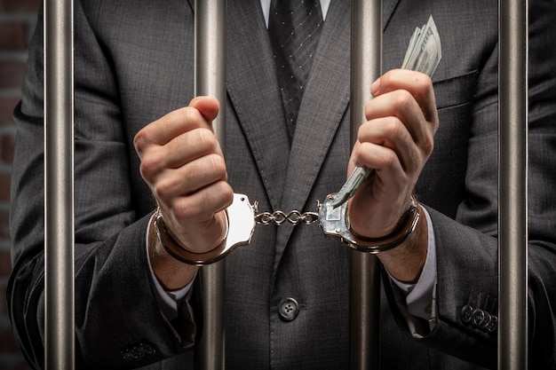 Business man holding bills of money with a handcuff in a jail. concept of corruption, corrupt politicians, illegal businesses. brick background.