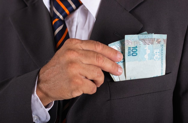 Деловой человек держит бразильские деньги в руке в кармане костюма.