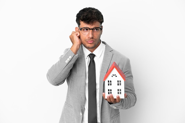 Business man holding a house isolated on blue background frustrated and covering ears