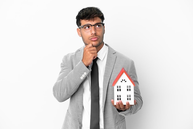 Business man holding a house isolated on blue background having doubts and thinking