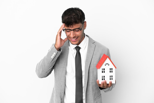 Business man holding a house isolated on blue background laughing